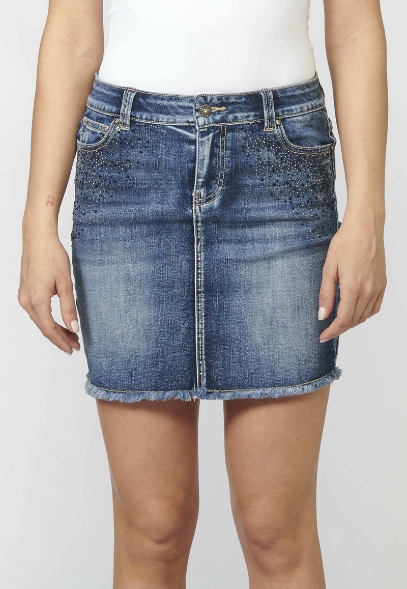 Mini-jupe en denim bleu foncé, avec un ourlet effiloché et des strass décoratifs à l'avant. Conception ajustée avec une taille standard.