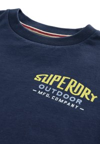 Marinblå bomulls-t-shirt med rundad nacke och en skärmtryckt logga i gult och vitt, med subtila texturdetaljer.