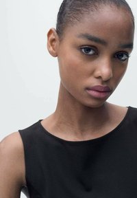 Close-up of a model with dark skin and sleek hair, wearing a black, sleeveless top. The fabric appears smooth with a slight sheen.
