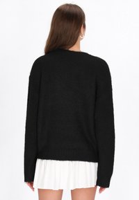 Czarny, oversize'owy sweter o miękkiej, teksturowanej powierzchni. Posiada długie rękawy i prążkowane wykończenie u dołu, noszony na białej plisowanej spódnicy.