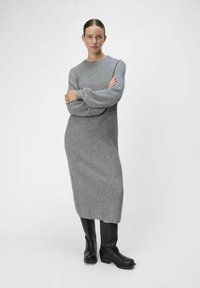 Abito grigio a costine con maniche lunghe, che arriva a metà polpaccio. Abbinato a stivali neri sopra il ginocchio, con suola spessa. Design semplice e minimalista.