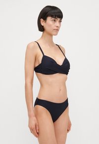 Črni bikini komplet, ki vsebuje textured wrap-stil zgornji del s tankimi naramnicami in usklajenim nizkim spodnjim delom. Preprost, minimalističen dizajn.