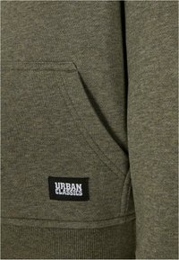 Felpa verde oliva realizzata in tessuto morbido, con tasca a marsupio, polsini a costine e etichetta 'Urban Classics' cucita di lato.