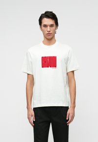 White cotton t-shirt with short sleeves featuring a red graphic print that includes the text "CALVIN KLEIN." Relaxed fit, crew neck design.