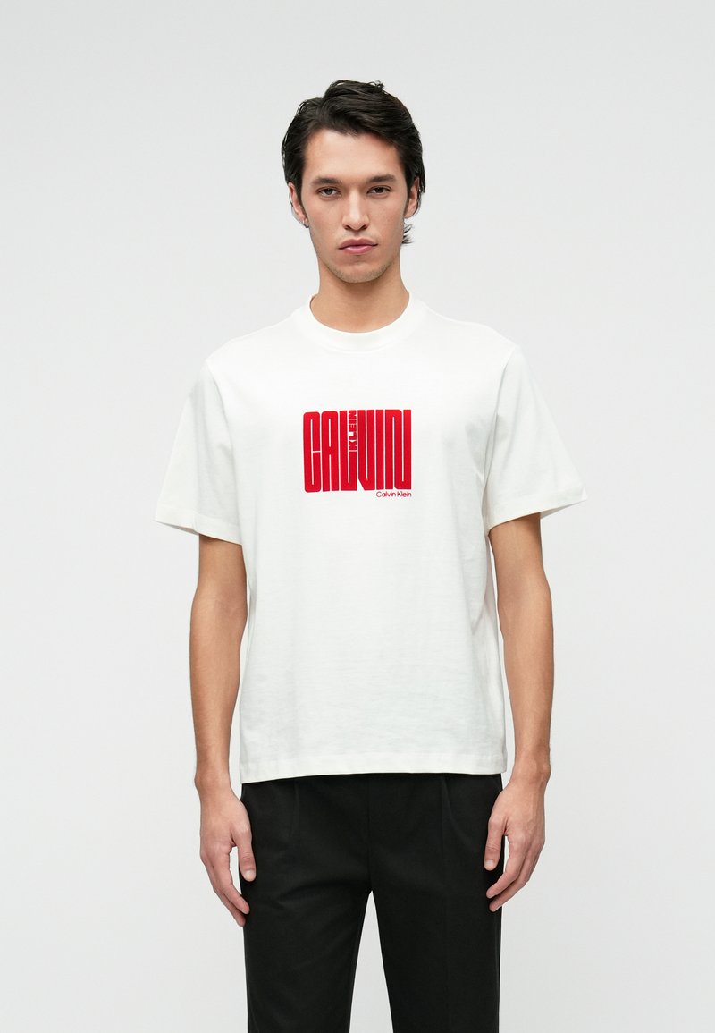 White cotton t-shirt with short sleeves featuring a red graphic print that includes the text "CALVIN KLEIN." Relaxed fit, crew neck design.