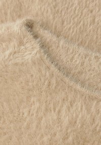 Beżowa, teksturowana tkanina o miękkim, puszystym wyglądzie. Posiada gładki dekolt oraz widoczne detale przeszycia.