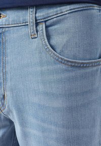 Jeans blu chiaro con un classico design a cinque tasche, realizzati in denim con una texture liscia, accentuati da cuciture dorate a vista.