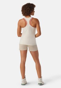 Helle beige Sporttanktop mit Racerback-Design und roten Akzenten, kombiniert mit hellbeigen Shorts und weißen Wanderschuhen.