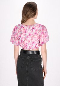 Kortærmet, lyserød blomstret bluse med snøret bund, parret med en højtaljet sort denimnederdel med baglommer.