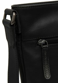 Borsa in pelle nera con zip superiore, finitura testurizzata, hardware argentato e etichetta con logo. Design semplice con tracolla regolabile.