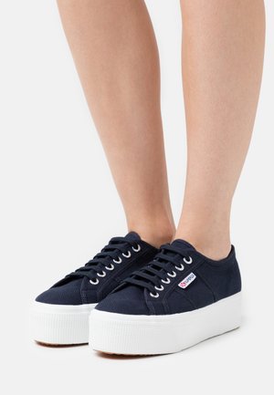 Navy canvas platform sneakers with white rubber soles, featuring white eyelets and laces, showcasing a textured surface and side branding.