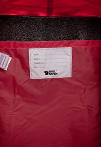 Intérieur en tissu rouge d'un sac, arborant une étiquette blanche avec des champs pour le nom, l'adresse, le code postal et le numéro de téléphone, marqué du logo Fjällräven.