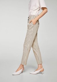 Pantaloni a righe in beige e grigio scuro, con vestibilità sartoriale, due tasche laterali e orlo con risvolto. Abbinati a décolleté bianche con cinturino.