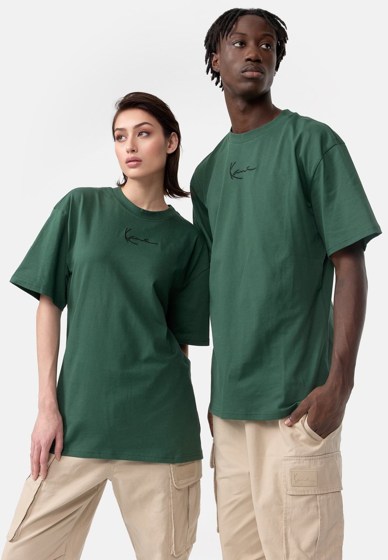 T-shirts en coton vert à manches courtes, ornés d'un petit logo noir sur la poitrine. Portés avec un pantalon cargo beige.