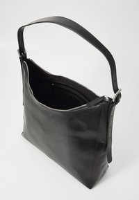 Sac fourre-tout en cuir noir avec une fermeture éclair, un corps plat et une longue bandoulière ajustable. Texture lisse et design minimaliste.