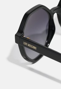 Μαύρα οκτάγωνα γυαλιά ηλίου με βαθμιαία φακούς. Διαθέτουν χρυσό λογότυπο "LOVE MOSCHINO" στο βραχίονα. Λείος πλαστικός φινίρισμα, παχύ σχεδιασμό σκελετού.