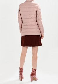Light pink puffer jacket with a high collar, quilted design, and fitted silhouette, paired with a brown skirt and pink velvet block-heeled ankle boots.