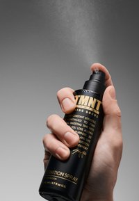 Svart sprayflaska med guldfärgad text och matt yta. Munstycket trycks ner och släpper ut en fin dimma i luften.