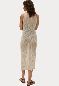 Abito senza maniche in maglia color beige chiaro con una vestibilità ampia, dotato di uno spacco posteriore e di un motivo testurizzato. Indossato sopra un costume da bagno.