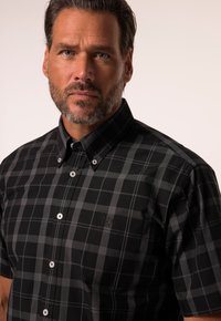Camicia a maniche corte a quadri in nero e grigio, realizzata in cotone, con chiusure a bottoni e un dettaglio con logo sulla tasca sinistra del petto.