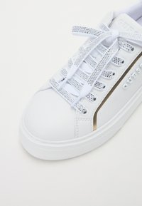 Sneakers bianchi con tomaia in pelle liscia, occhielli in tonalità argento, lacci argentati scintillanti e una striscia dorata sul lato.