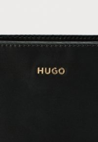 Portefeuille en cuir noir avec un logo "HUGO" doré. Texture lisse avec des coutures précises sur les bords, design minimaliste.