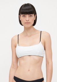 Witte bikini top met dunne zwarte bandjes, met een vierkante halslijn en een gladde, elastische textuur; gecombineerd met zwarte bikini onderbroek.