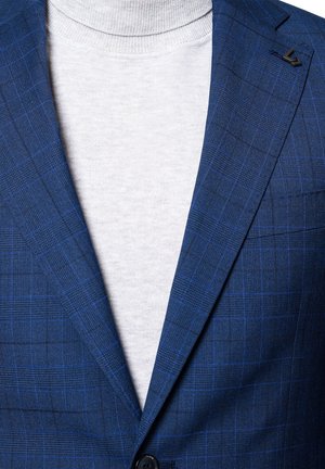 Granatowa marynarka w kratę z cienkimi niebieskimi liniami, na dwa guziki, z czarnym akcentem na klapie, nałożona na jasnoszary sweter z golfem.