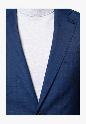 Granatowa marynarka w kratę z cienkimi niebieskimi liniami, na dwa guziki, z czarnym akcentem na klapie, nałożona na jasnoszary sweter z golfem.