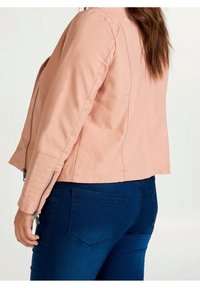 Różowa kurtka z ekologicznej skóry o dopasowanym kroju, z bocznym zamkiem i pikowanymi detalami na ramionach, zestawiona z ciemnoniebieskimi jeansami.