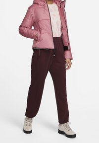 Rosa puffjacka med huva, dragkedjeslutning och vadderad design. I kombination med vinröda sweatpants och beige snörstövlar.