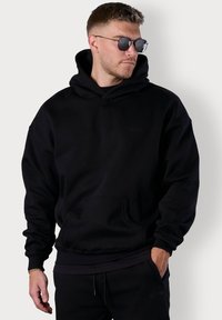 Black hooded sweatshirt made of fleece fabric, featuring a front kangaroo pocket, ribbed cuffs, and a minimal embossed logo.