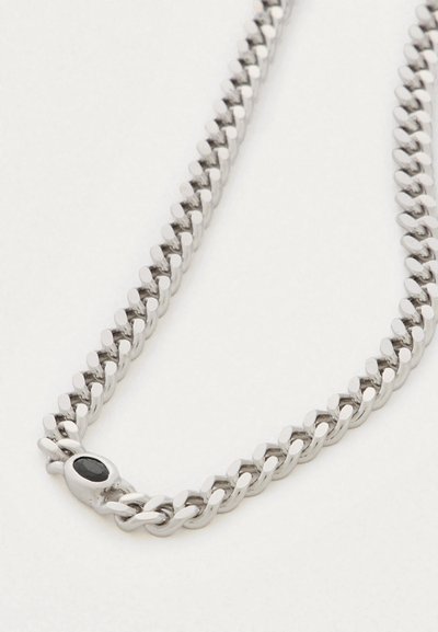 Detailní záběr stříbrného náhrdelníku s tlustými propletenými články a černým oválným zapínáním na bílém pozadí.