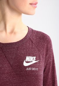 Bordeaux dlouhý rukáv s kulatým výstřihem, se bílým logem Nike a textem "JUST DO IT". Texturovaná tkanina s melírovaným vzhledem.