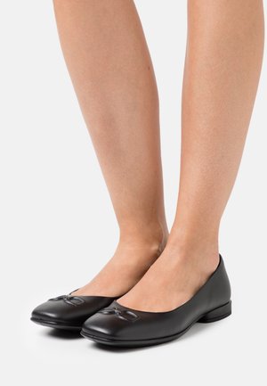 Ballerines en cuir noir avec un bout arrondi, ornées d'un petit nœud sur le devant et d'un petit talon rond. Texture lisse.