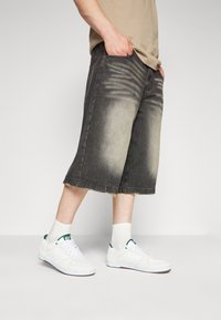 Shorts de mezclilla en tonos negro y gris deslavados con dobladillo deshilachado, combinados con zapatillas blancas y calcetines blancos. Tejido texturizado con coloración degradada.