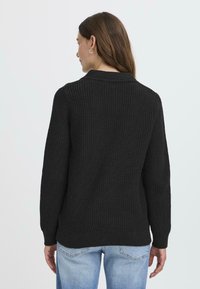 Pull en tricot noir avec texture côtelée, manches longues et coupe décontractée. Il présente un col rond et un ourlet droit.