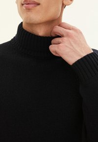Maglione a collo alto lavorato a maglia nera con texture a coste, caratterizzato da un collo alto e maniche lunghe, aderente al collo e ai polsini.