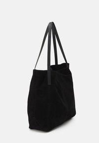 Zwarte suède tas met dubbele platte handvaten, zachte textuur, open bovenkant en driehoekige hoeken. Minimalistisch ontwerp zonder zichtbare hardware.