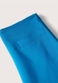 Tissu bleu affichant une texture lisse, avec une poche horizontale cousue sur la surface, pliée au bord supérieur.