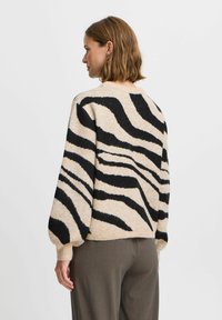 Beez žakett mustade zebra triipudega, ümmarguse kaelusega ja puhvis varrukatega. Seljas hallid püksid, rõhutades lõdva istuvust.