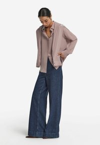 Jasnoróżowa koszula zapinana na guziki, pod którą znajduje się dopasowana różowa kurtka; szerokie ciemnoniebieskie dżinsy o czystych nogawkach; gładkie tekstury tkanin.