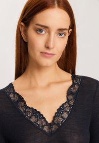 Maglia a maniche lunghe navy con scollatura a V in pizzo. Presenta una texture a coste e un raffinato bordo in pizzo floreale lungo il colletto.