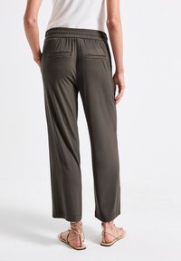 Pantaloni larghi verde scuro, con vita elastica e due tasche posteriori, abbinati a sandali piatti color beige. Tessuto dalla texture liscia.