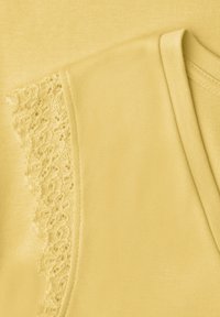 Tissu jaune montrant un gros plan d'un vêtement avec une bordure en dentelle et un bord plié, mettant en avant la texture et les détails de la couture.