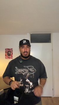 Must graafiline T-särk valge tekstiga, kantud musta pesapalli nokamütsiga. Hele taust plakatiga seinal, nähtav puidust põrand.