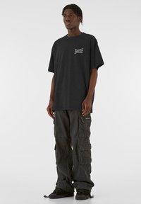 Sort oversized T-shirt med minimal grafisk accentuerede detaljer, parret med mørke cargo bukser med flere lommer og sorte sneakers.