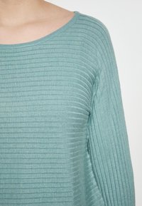 Maglietta a maniche lunghe azzurro chiaro a coste con scollatura rotonda e texture morbida, caratterizzata da strisce verticali uniformi su tutta la stoffa.