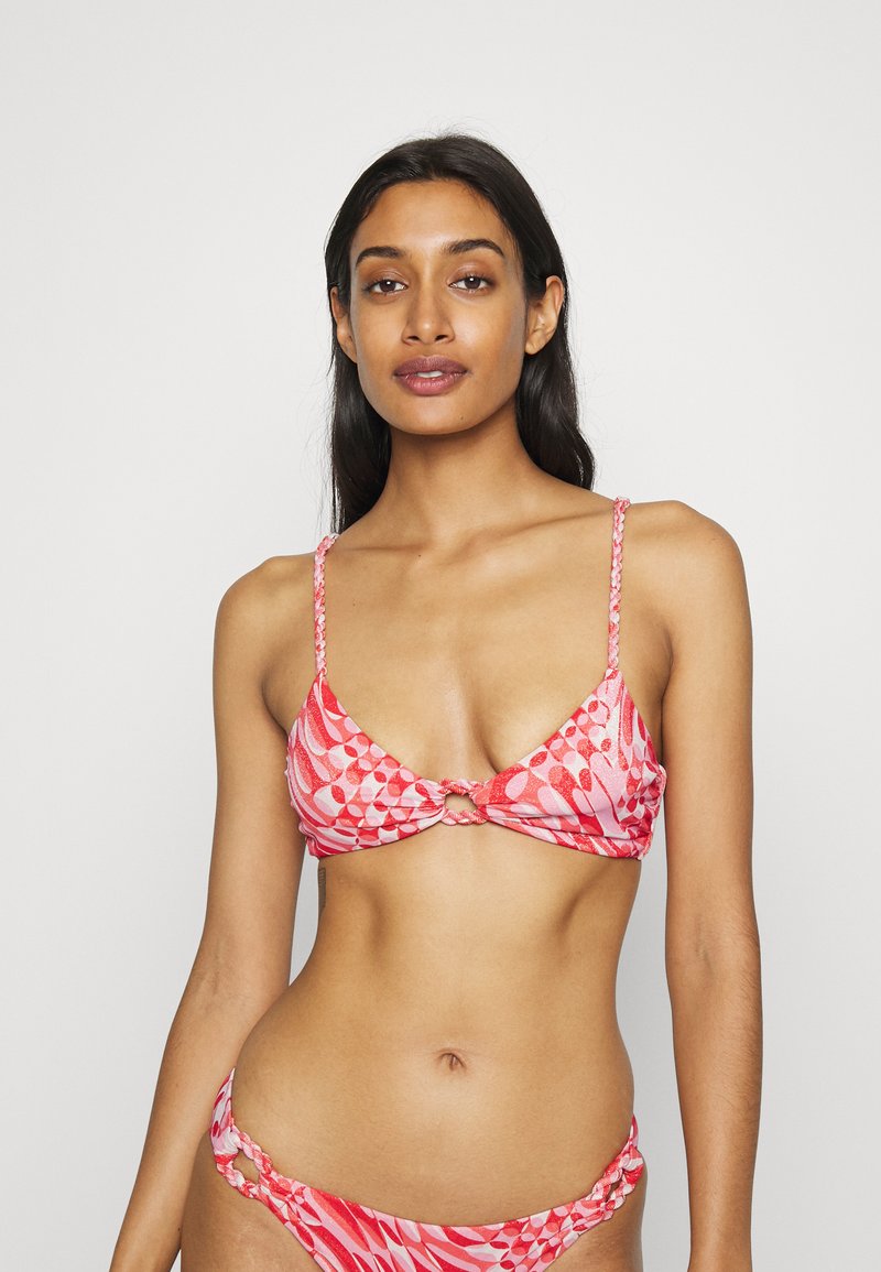 Bikini em padrões rosa e vermelho com um centro atado, tiras finas trançadas e detalhes em metal nas cuecas. Textura de tecido suave.
