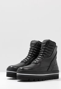 Botas de tobillo negras con una parte superior de piel lisa, detalles acolchados, cuello acolchado y suela gruesa negra con franjas blancas.